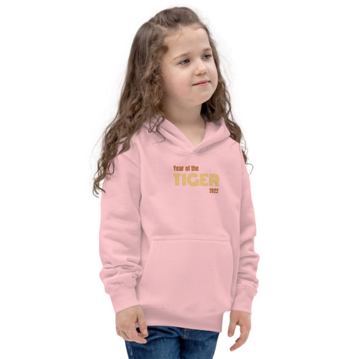 A girl with long wavy brown hair is looking off to the side. She is wearing a pink hoodie that says "year of the Tiger 2022" and jeans