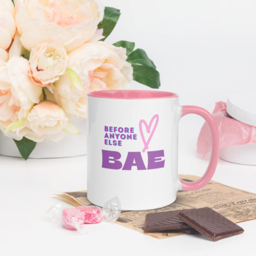 a coffee mug with purple text saying " BAE, Before Anyone Else" and a heart. The Mug is white at the is a pink handle with pink inside. There are pink roses in the background and chocolates and candy at the bottom