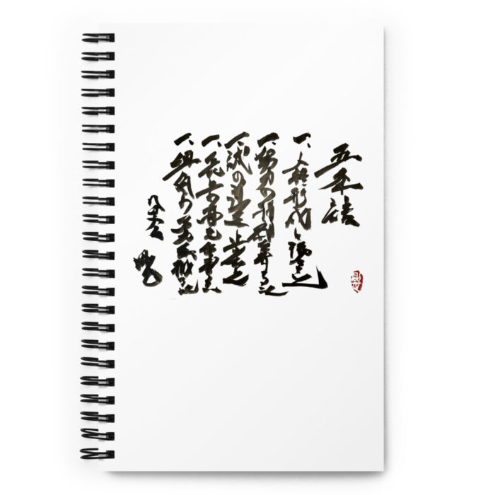 A white notebook with Japanese Calligraphy, the Calligraphy is the "Dojo" Kun (rules) It is black spiral bound