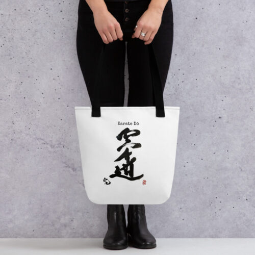 A woman, who is only shown from the hips down, she is wearing black leggings ad black Doc-like boots. She is carrying a White Tote bag with black handles and there is Japanese Calligraphy on the Top that says Karate Do